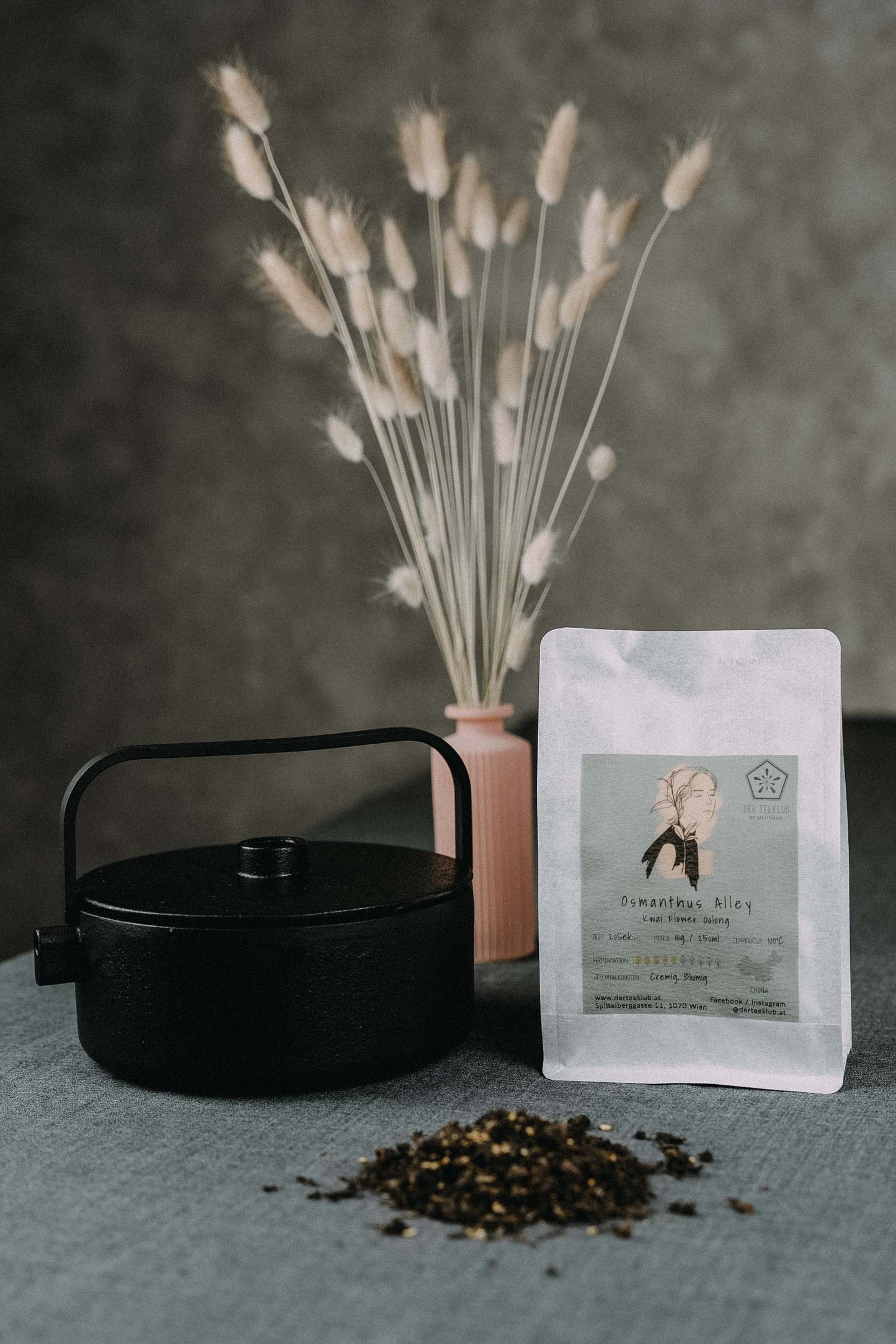 dunkler Oolongtee mit gelben Osmanthusblüten neben großer Kanne